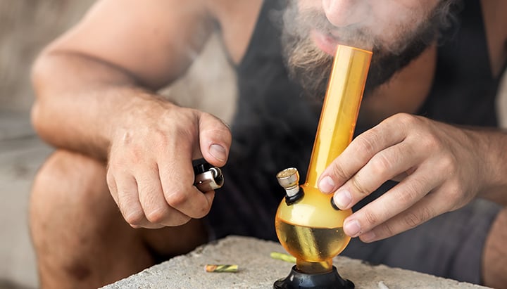 Person smoking hash from a glass bong, exhaling thick smoke. 