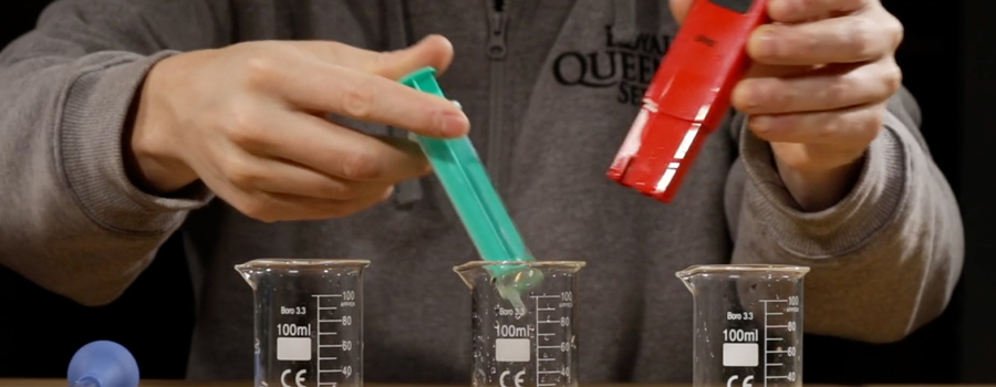 Person testing liquid pH using a pH meter and syringe. The syringe is about to be inserted into a beaker, with two other beakers visible on the table, for a pH measurement process.