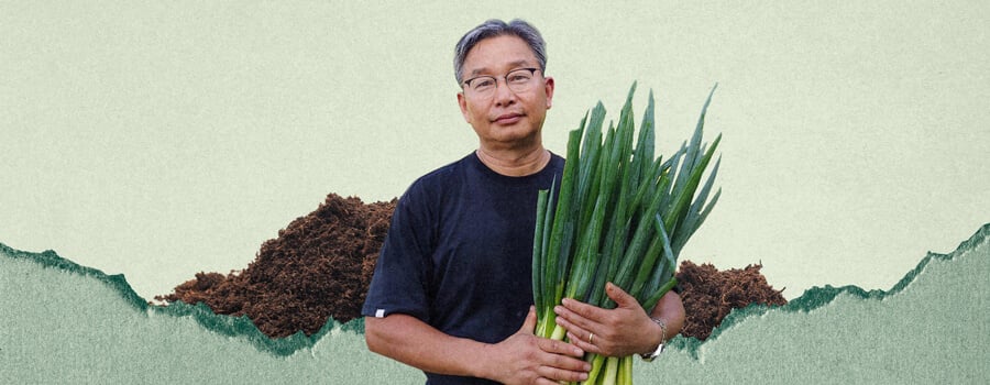 A man named Youngsang Cho is holding a bunch of green onions. He is standing in front of a pile of dirt.