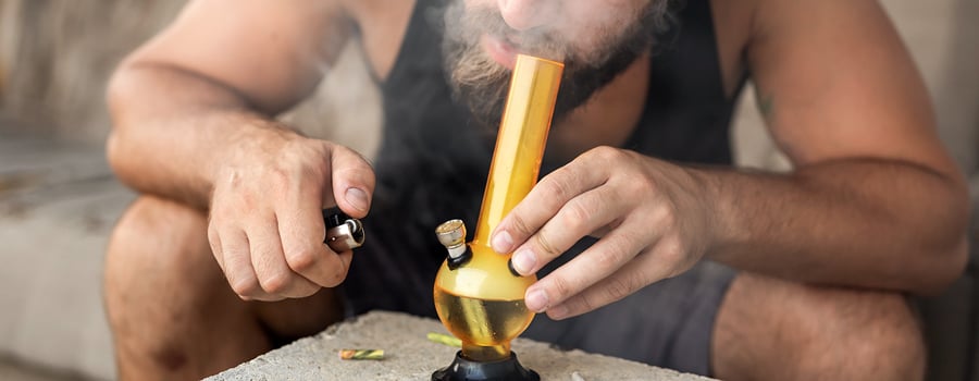 Person smoking hash from a glass bong, exhaling thick smoke. 